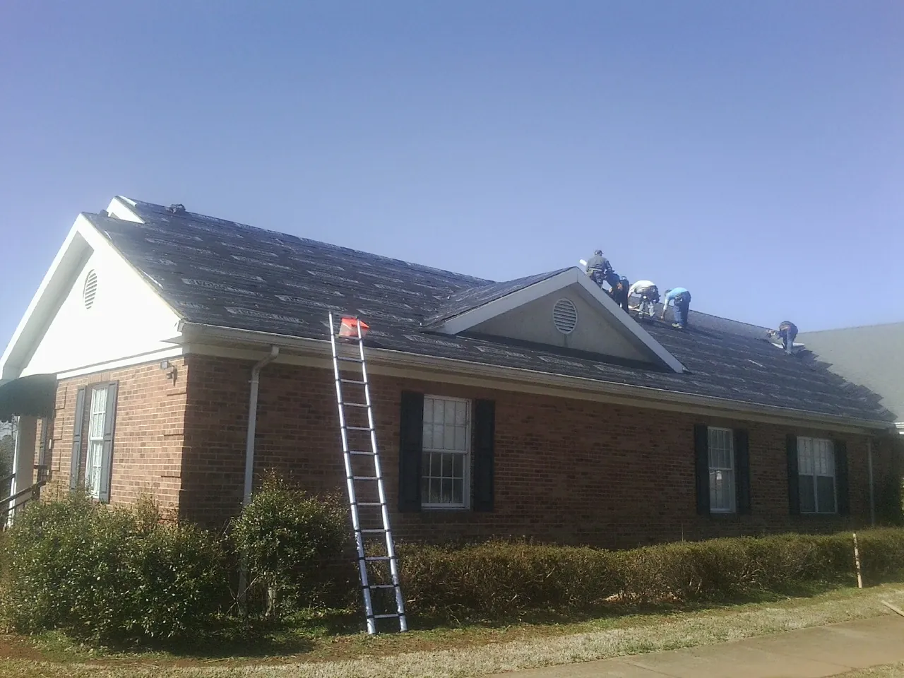 Crew tearing shingles off a brick ranch roof with a ladder set — Emergency Roof Repair work by our crew in West Union