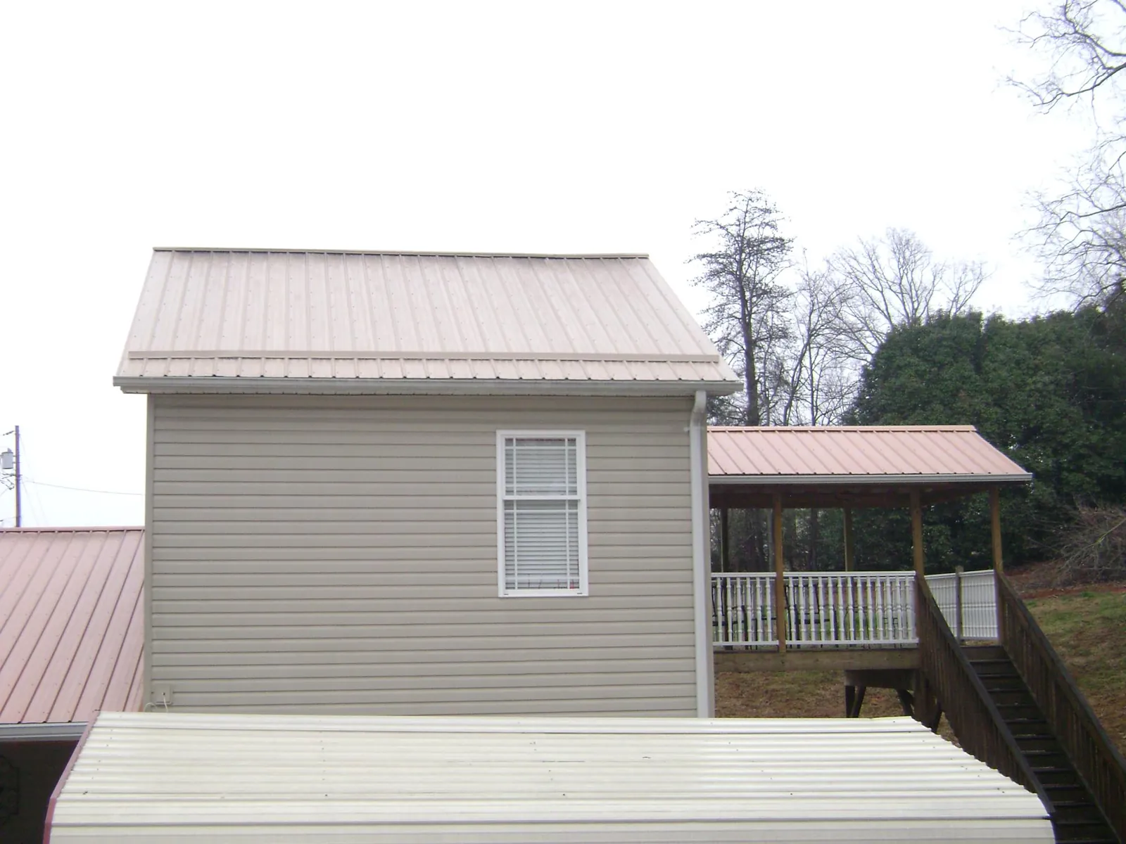 Tan metal roofs on a two story addition and attached porch, from a Roof Replacement job in West Union